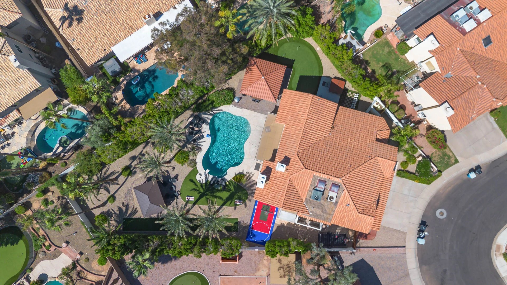 Aerial view of a finished backyard with pool, sport court and putting green